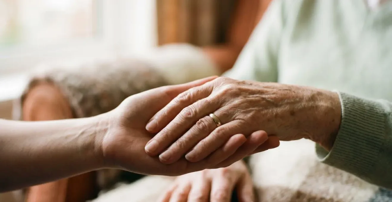 Close portrait of an elderly person's hand being gently held by a caregiver's hand showing human connection and non-verbal communication in dementia care