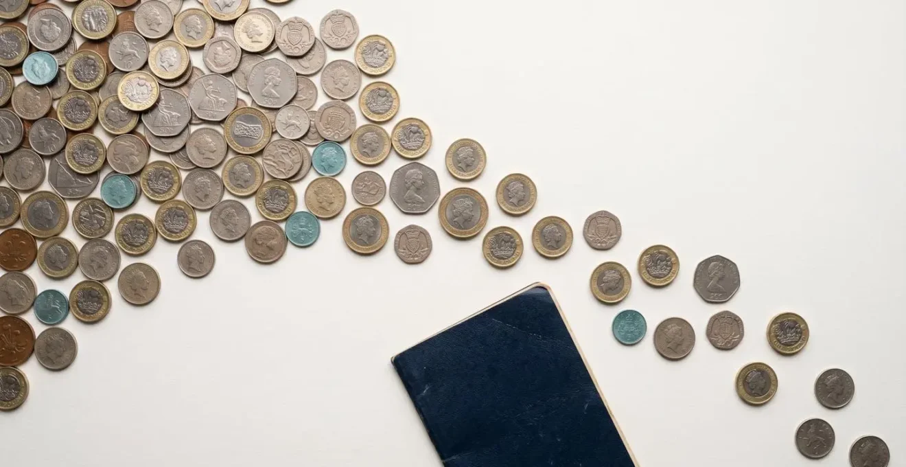 Minimalist overhead view of British coins and savings passbook on clean white surface
